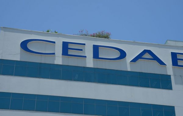 Na imagem, encontra-se a fachada da Companhia Estadual de Águas e Esgotos do Rio de Janeiro. A logo azul é em azul e em letras maiúsculas. O prédio é pintado de branco, com faixas azuis horizontais.